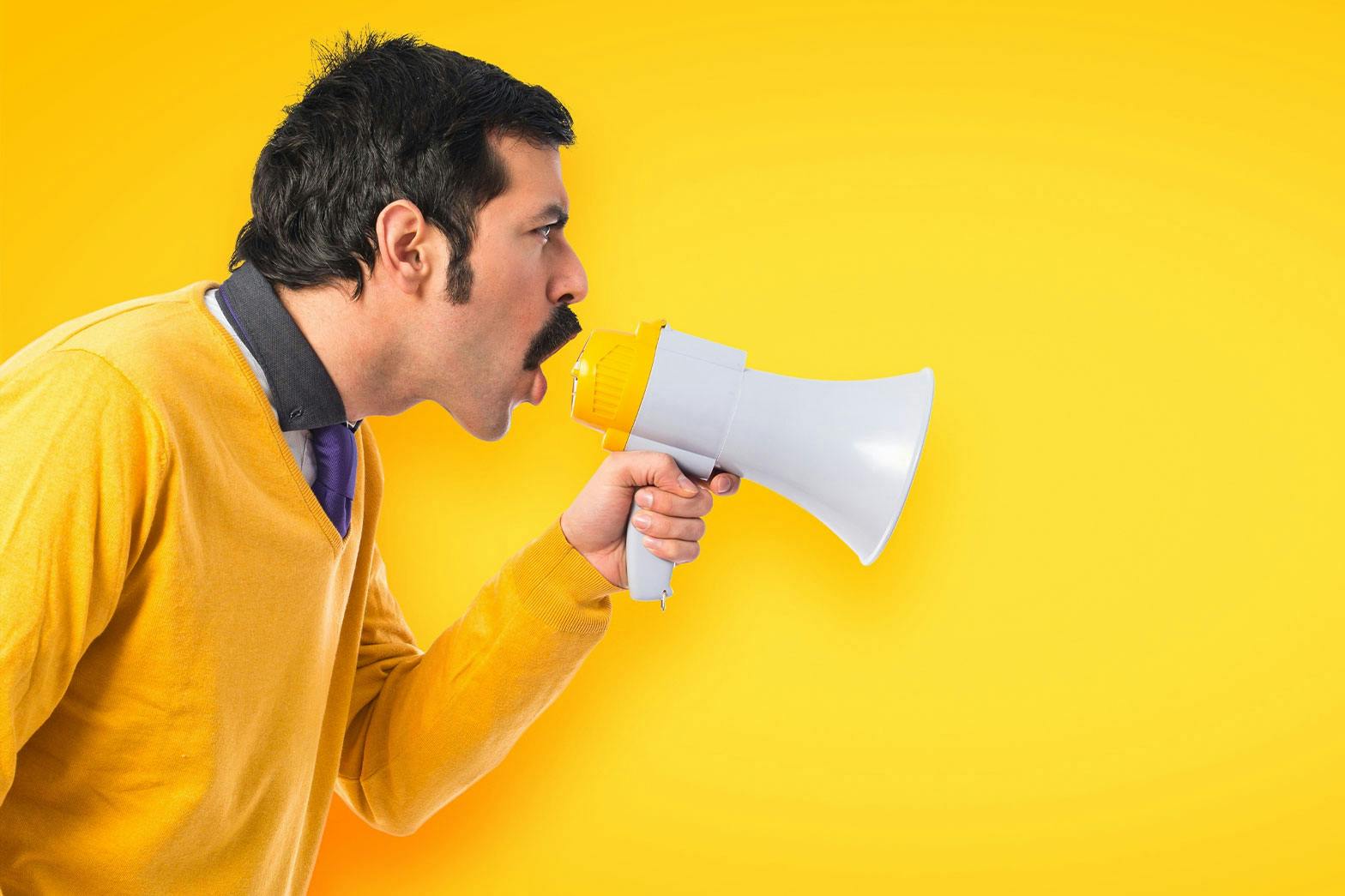 A man in yellow yelling in to a megaphone