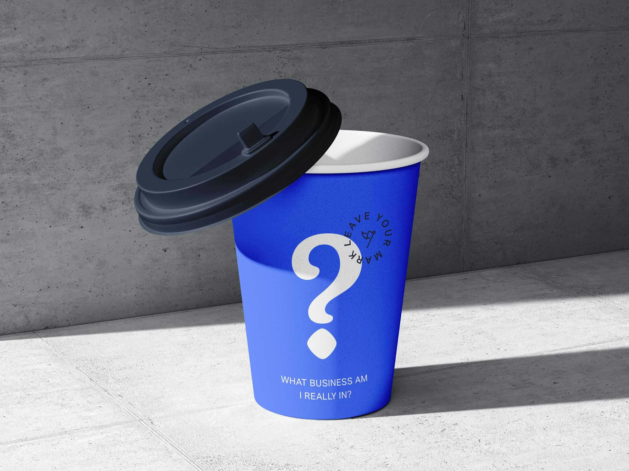 A blue coffee takeaway cup on a concrete background with a question mark and words saying what business are you really in?