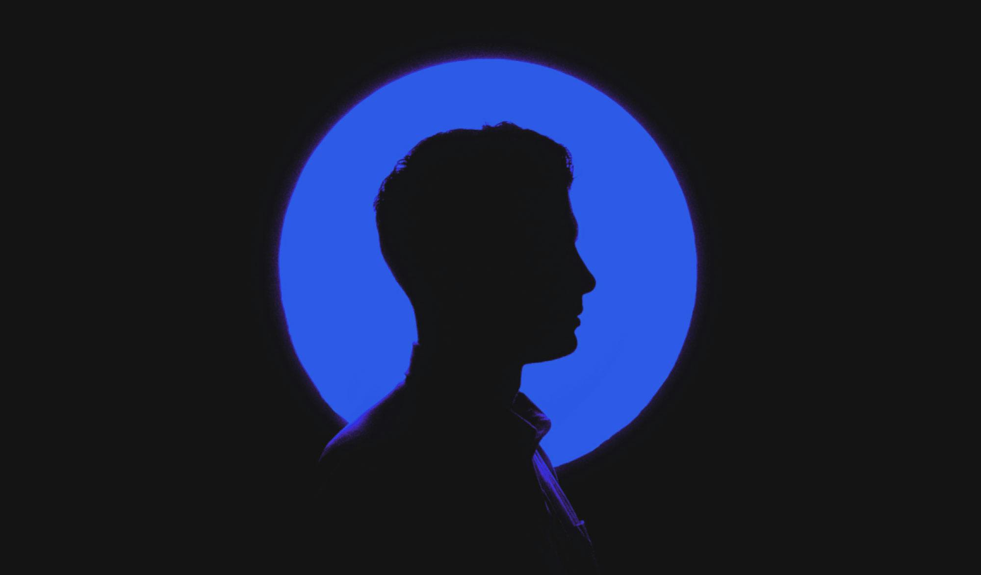 Silhouette of a mans profile behind a blue circle light on a black background.